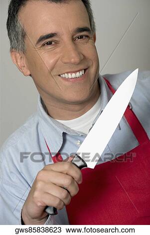 Stock Image - Portrait of a mid adult man holding a kitchen knife and smiling. Fotosearch