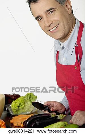 Stock Image - Portrait of a mid adult man holding a knife in front of vegetables. Fotosearch