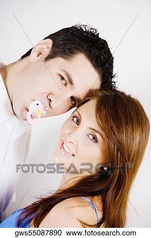 Stock Image - Portrait of a mid adult man sucking a pacifier with a young woman smiling. Fotosearch