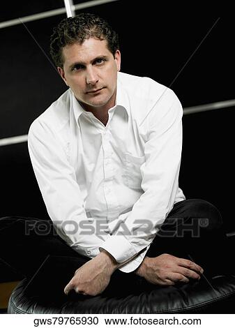 Stock Image - Portrait of a mid adult man with sitting with his legs crossed. Fotosearch