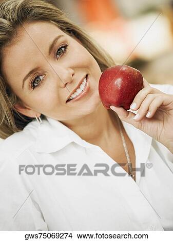 Picture - Portrait of a mid adult woman holding an apple and smiling. Fotosearch