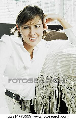 Stock Photo - Portrait of a mid adult woman leaning against a bed and smiling. Fotosearch