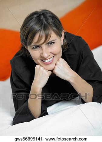 Stock Image - Portrait of a mid adult woman lying on the bed with her hand on her chin. Fotosearch