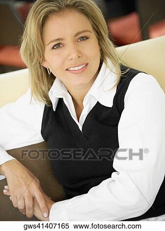 Portrait of a mid adult woman sitting on a couch and smiling View Large Photo Image Stock Photography - Portrait of a mid adult woman sitting on a couch and smiling. Fotosearch