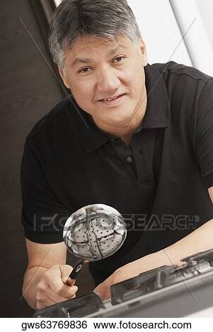 Stock Photograph - Portrait of a senior man holding a ladle over a burner and smiling. Fotosearch