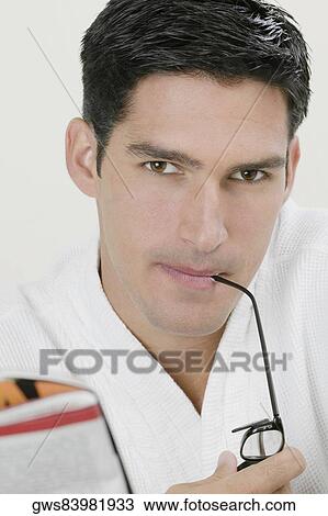 Stock Image - Portrait of a young man biting the shaft of his eyeglasses. Fotosearch