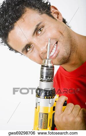 Stock Photograph - Portrait of a young man holding a drill machine and smiling. Fotosearch