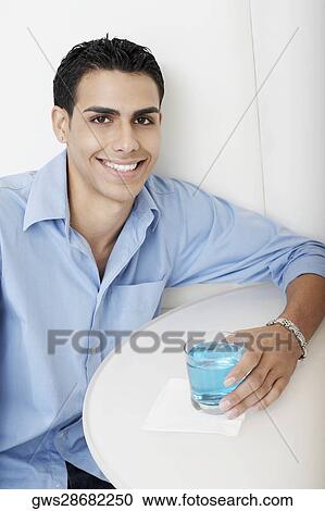 Stock Image - Portrait of a young man holding a cocktail and smiling. Fotosearch