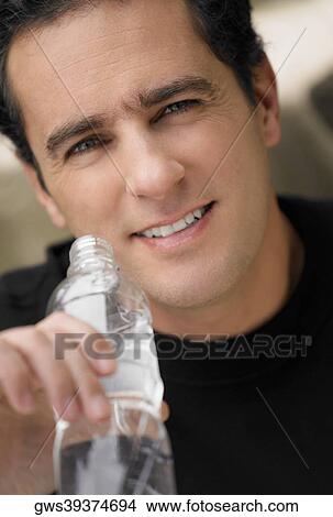Picture - Portrait of a young man holding a water bottle and smiling. Fotosearch