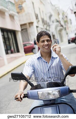 Stock Image - Portrait of a young man riding a motor scooter and talking on a mobile phone. Fotosearch