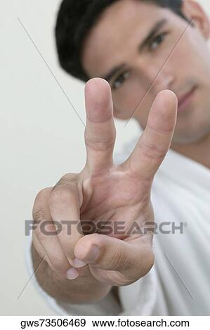 Stock Photo - Portrait of a young man showing a peace sign. Fotosearch