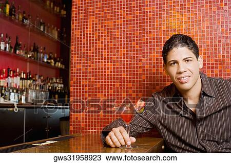 Portrait of a young man sitting at a bar counter holding a cocktail View Large Photo Image Stock Image - Portrait of a young man sitting at a bar counter holding a cocktail. Fotosearch