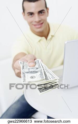 Portrait of a young man sitting in front of a laptop and holding one hundred dollar bills View Large Photo Image Stock Image - Portrait of a young man sitting in front of a laptop and holding one hundred dollar bills. Fotosearch