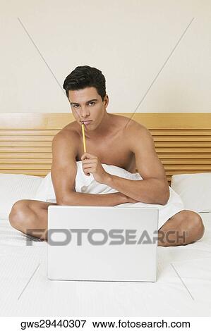 Portrait of a young man sitting on the bed with a laptop View Large Photo Image Stock Photo - Portrait of a young man sitting on the bed with a laptop. Fotosearch