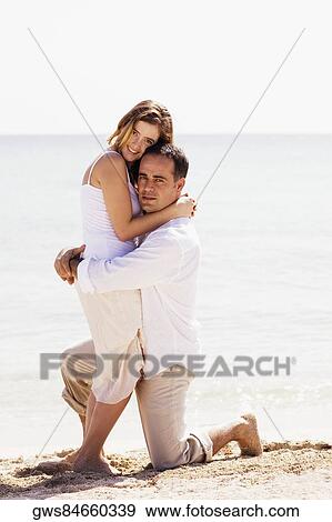 Stock Photo - Portrait of a young woman and a mid adult man embracing each other on the beach. Fotosearch