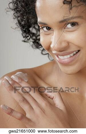 Stock Image - Portrait of a young woman applying moisturizer on her shoulder and smiling. Fotosearch