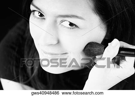 Stock Photograph - Portrait of a young woman applying blush with a brush. Fotosearch