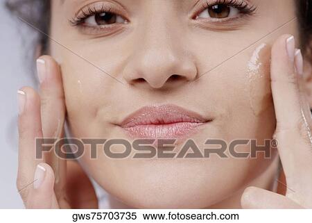 Portrait of a young woman applying moisturizer on her cheeks View Large Photo Image Stock Photography - Portrait of a young woman applying moisturizer on her cheeks. Fotosearch