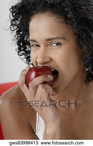 Stock Image - Portrait of a young woman eating an apple. Fotosearch