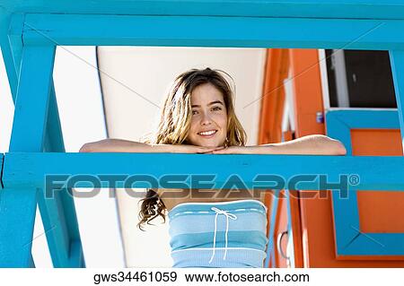 Stock Photo - Portrait of a young woman leaning against a railing and smiling. Fotosearch