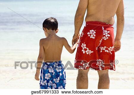 Rear view of a boy holding his father's hands standing on the beach View Large Photo Image Stock Image - Rear view of a boy holding his father's hands standing on the beach. Fotosearch