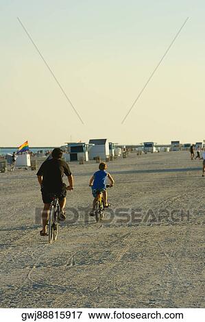 Rear view of a man and a child cycling on the beach View Large Photo Image Stock Photo - Rear view of a man and a child cycling on the beach. Fotosearch