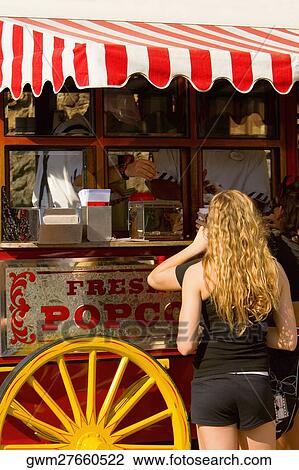 Stock Image - Rear view of a man and a woman buying popcorn from a market stall. Fotosearch