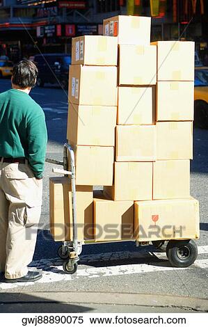 Stock Photography - Rear view of a man standing near a push cart with cardboard boxes. Fotosearch
