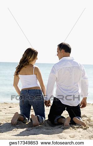Rear view of a mid adult man and a young woman kneeling with holding hands on the beach View Large Photo Image Stock Image - Rear view of a mid adult man and a young woman kneeling with holding hands on the beach. Fotosearch