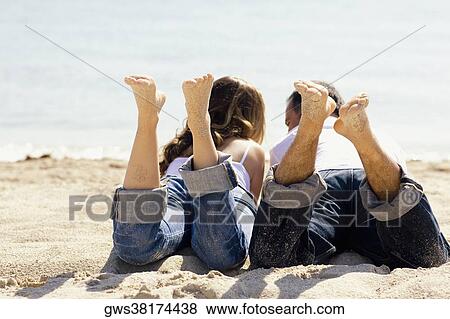 Stock Photo - Rear view of a mid adult man and a young woman lying on the beach. Fotosearch