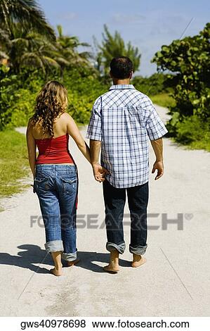 Rear view of a mid adult man and a young woman walking and holding hands in a park View Large Photo Image Stock Photo - Rear view of a mid adult man and a young woman walking and holding hands in a park. Fotosearch