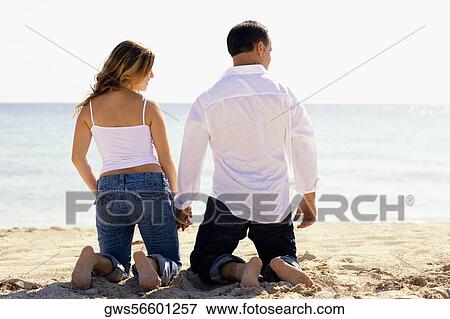 Rear view of a mid adult man and a young woman kneeling with holding hands on the beach View Large Photo Image Stock Photo - Rear view of a mid adult man and a young woman kneeling with holding hands on the beach. Fotosearch