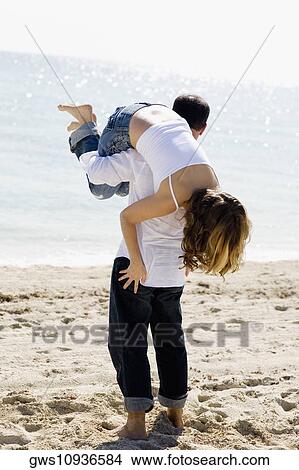 Picture - Rear view of a mid adult man carrying a young woman on his shoulder. Fotosearch