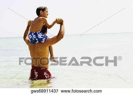 Rear view of a mid adult man carrying his son on his shoulders on the beach View Large Photo Image Stock Photo - Rear view of a mid adult man carrying his son on his shoulders on the beach. Fotosearch