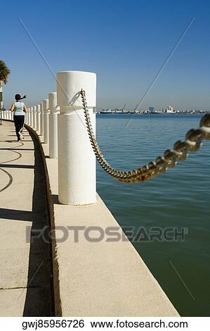 Stock Photograph - Rear view of a woman jogging on the sidewalk along the sea, Miami, Florida, USA. Fotosearch