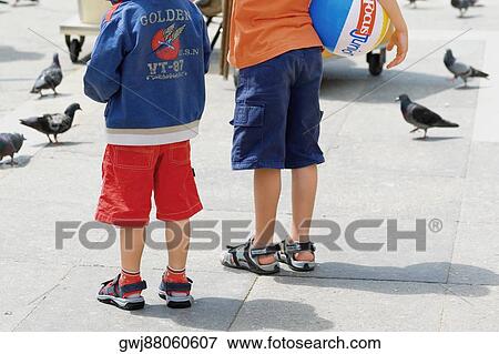 Stock Photo - Rear view of two children standing beside pigeons, Venice, Veneto, Italy. Fotosearch