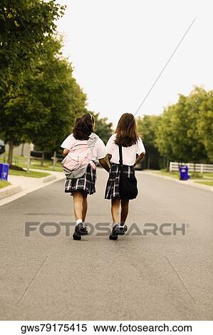 Stock Photography - Rear view of two schoolgirls walking on the road. Fotosearch