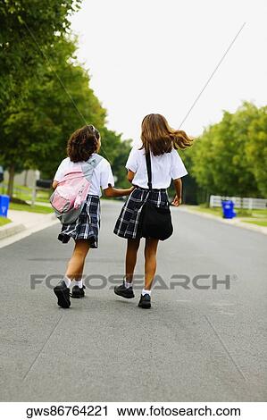 Stock Image - Rear view of two schoolgirls walking with holding hands. Fotosearch
