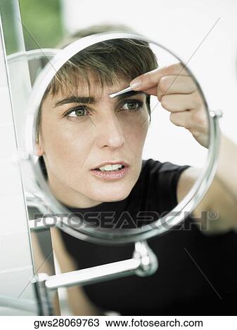 Reflection of a mature woman tweezing her eyebrows in a mirror View Large Photo Image Stock Image - Reflection of a mature woman tweezing her eyebrows in a mirror. Fotosearch