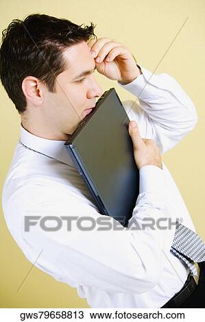 Stock Image - Side profile of a businessman holding a laptop and thinking. Fotosearch