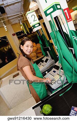Stock Image - Side profile of a girl using a cash register at the checkout counter. Fotosearch