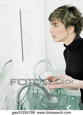 Side profile of a mature woman holding a bar of soap in front of a mirror in the bathroom View Large Photo Image Stock Photo - Side profile of a mature woman holding a bar of soap in front of a mirror in the bathroom. Fotosearch