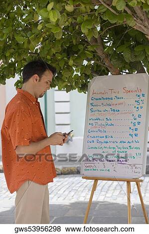 Stock Photo - Side profile of a mid adult man standing in front of a menu and holding a mobile phone. Fotosearch