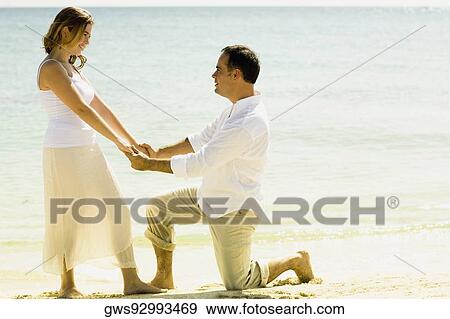 Side profile of a mid adult man kneeling in front of a young woman on the beach View Large Photo Image Stock Photo - Side profile of a mid adult man kneeling in front of a young woman on the beach. Fotosearch