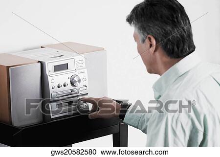 Stock Image - Side profile of a senior man playing a CD player. Fotosearch