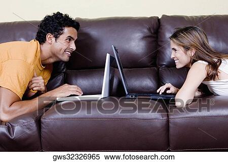 Side profile of a young couple lying on a couch and using laptops View Large Photo Image Stock Photography - Side profile of a young couple lying on a couch and using laptops. Fotosearch