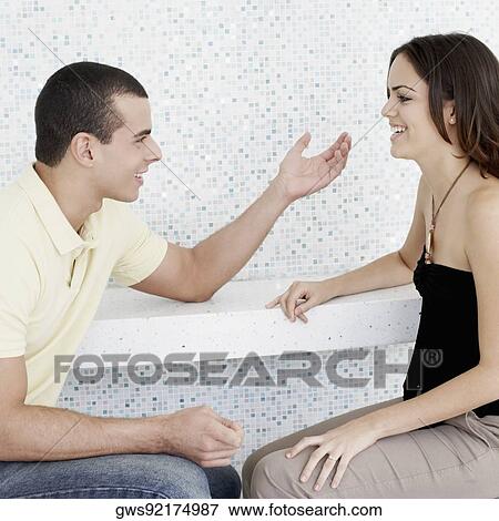 Stock Photo - Side profile of a young couple talking to each other. Fotosearch
