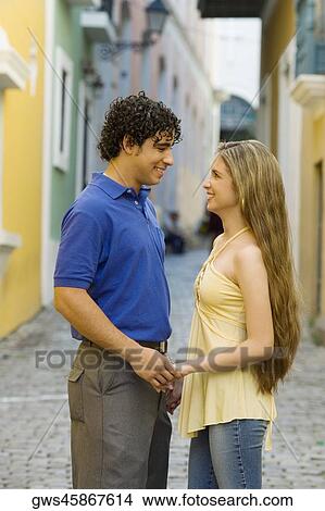 Picture - Side profile of a young man and a teenage girl standing face to face on the street. Fotosearch