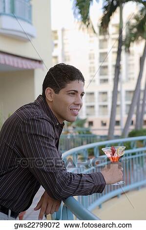Side profile of a young man leaning against a railing and holding a cocktail View Large Photo Image Stock Image - Side profile of a young man leaning against a railing and holding a cocktail. Fotosearch