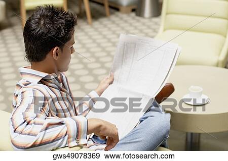Side profile of a young man sitting on a couch and reading a newspaper View Large Photo Image Stock Photo - Side profile of a young man sitting on a couch and reading a newspaper. Fotosearch
